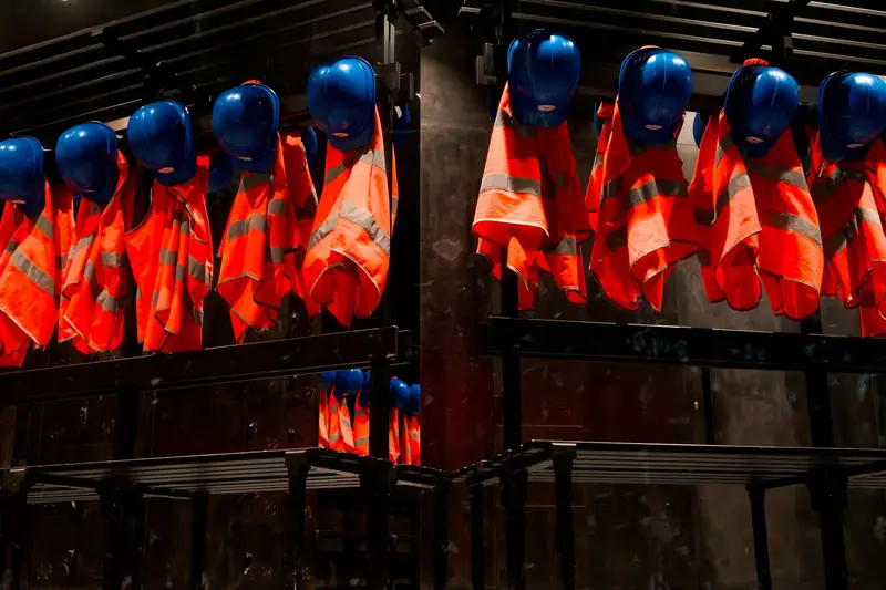 Rows of hi-vis vests and hard hats hanging on a site rack