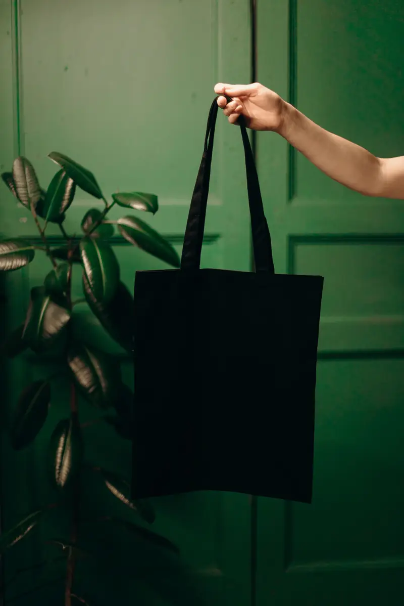 Black canvas tote bag held up against a green wall